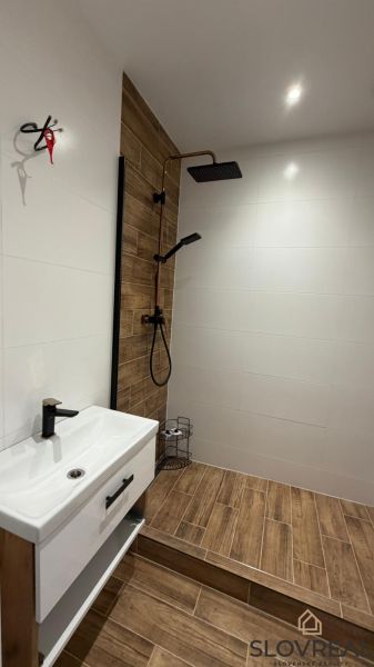 A bathroom in a 3-room apartment with a wooden decor floor and a shower corner.