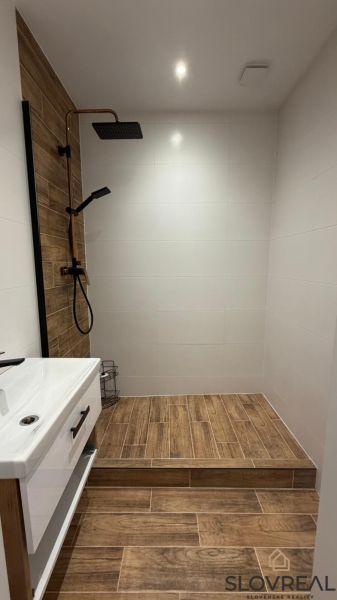 A modern bathroom in a 3-room apartment with a wooden decor floor and a shower corner.