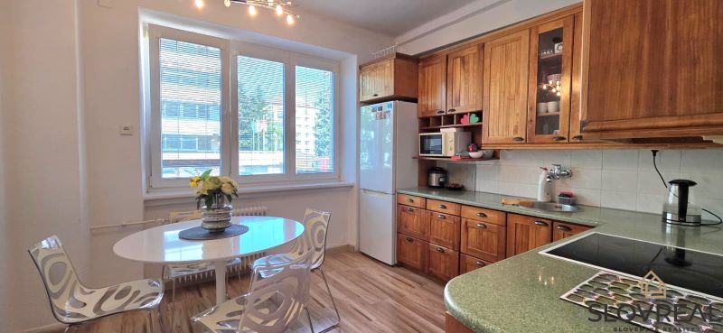 A kitchen in a 2-room apartment with a light table, wooden cabinets, and a floor with a wooden decor.
