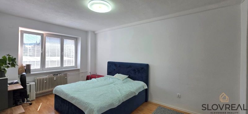 A bedroom with a bed, a work desk, and a floor with a wooden decor in a two-room apartment.