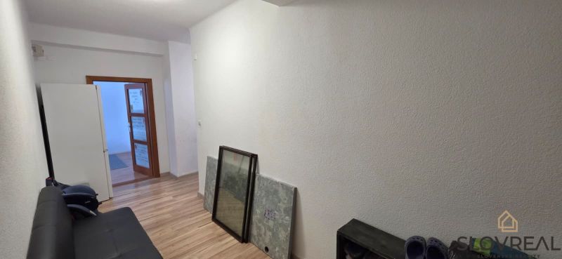 A narrow corridor with a sofa, a wooden decor floor, and open doors in a 2-room apartment.
