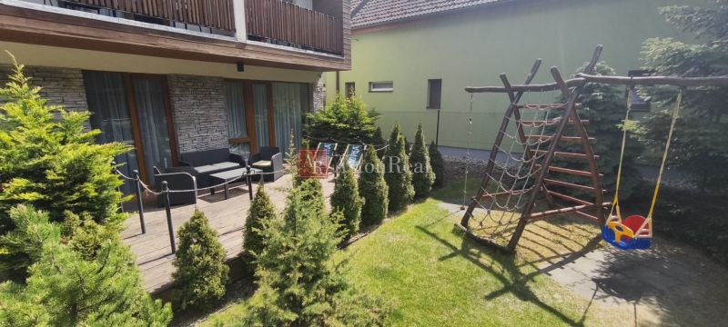 The courtyard of a recreational apartment in Demänová with a terrace, a playground, and green conifers.