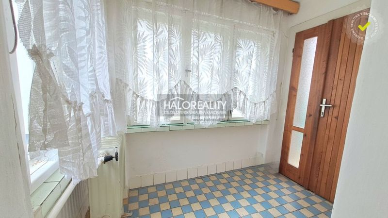 A small hallway in a family house with a tiled floor and curtains on the window.