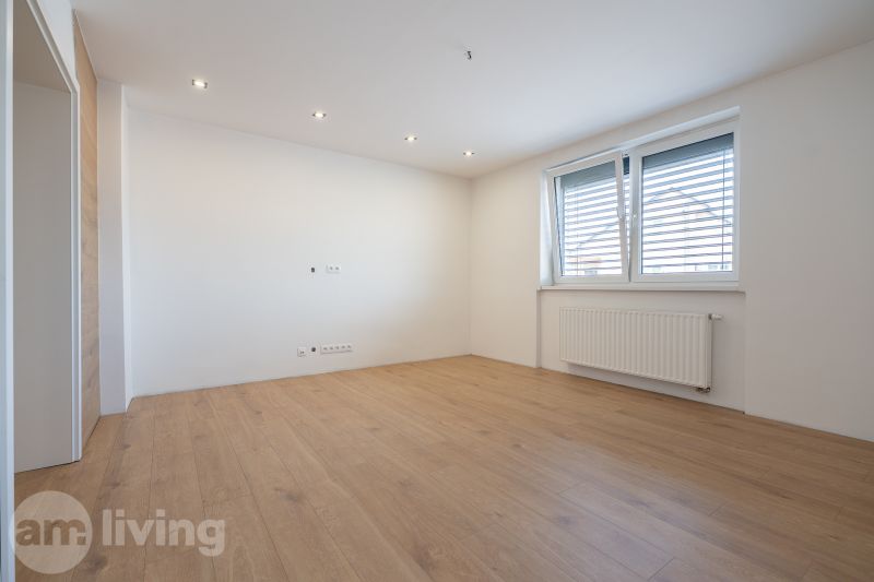 Interior of a family house with a wooden decor floor, white walls, and a window.