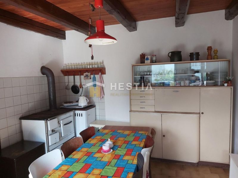 A dining room with a tiled stove, an old sideboard, and a colorful tablecloth on the table.