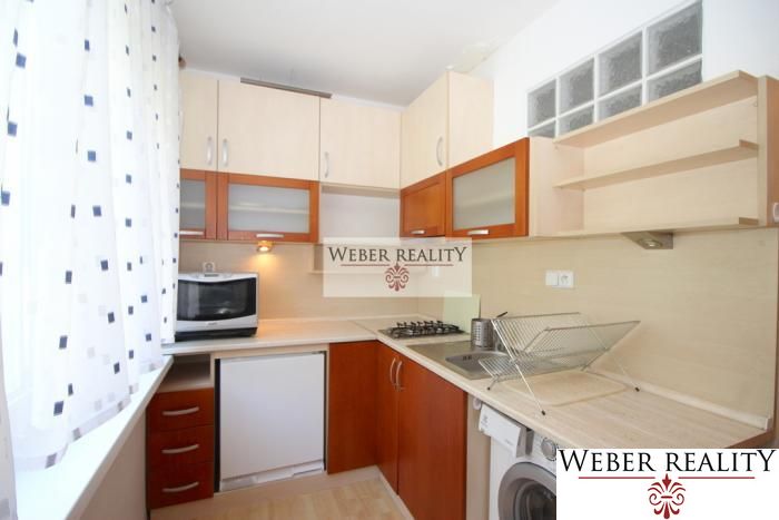 A kitchen in a studio apartment with a microwave, a gas stove, and a wooden decor floor.
