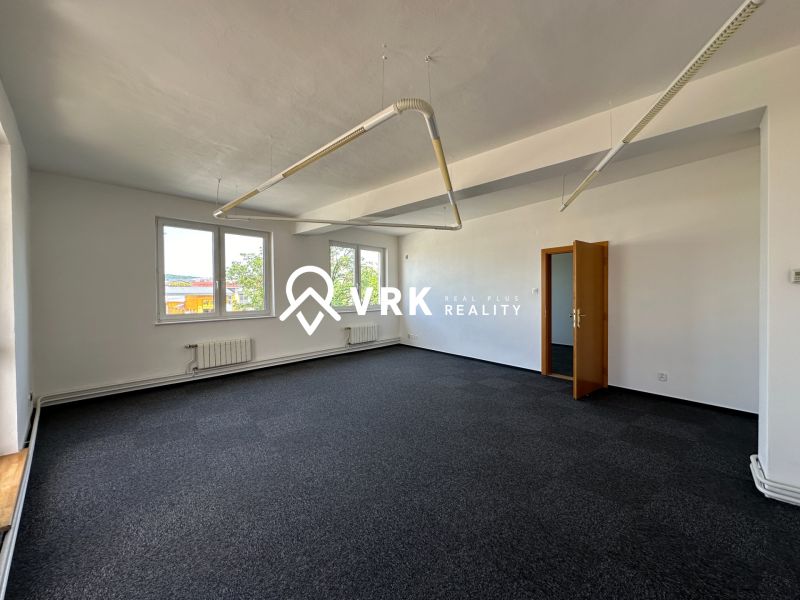 A spacious office with carpeted flooring and white walls, equipped with pendant lighting.