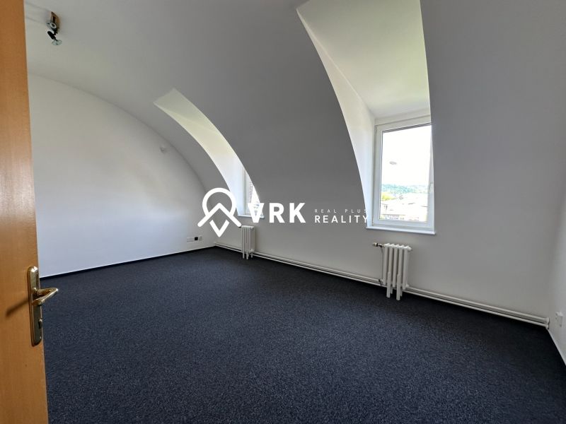 Office space with a curved ceiling and carpet, equipped with a radiator and a window.