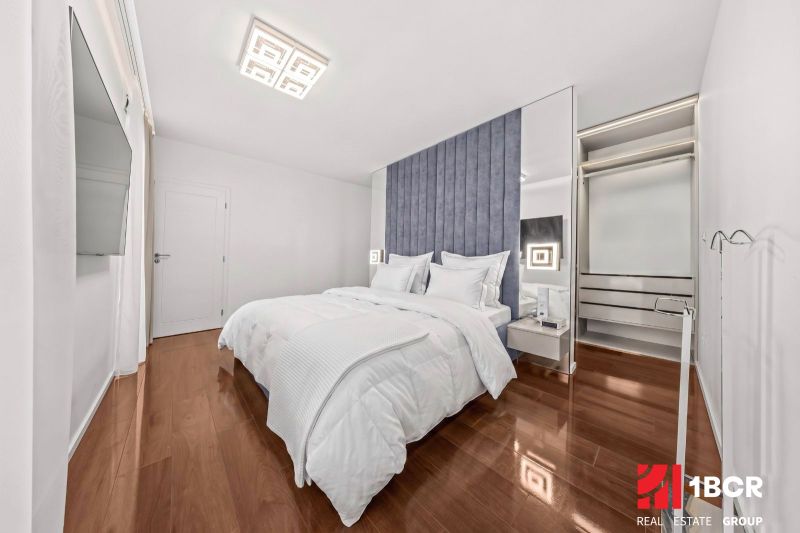 A bright bedroom with a blue headboard, a television, and a wooden decor floor in a family house.