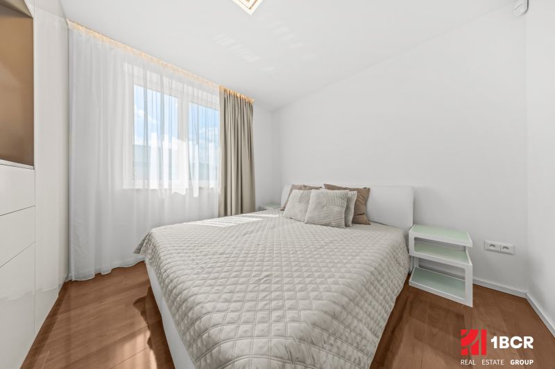 A bedroom with a large bed, white walls, and a wood-patterned floor in a family house.