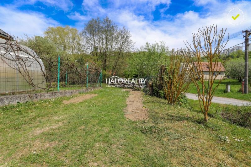 Gardens in Považská Bystrica with a grassy area, trees, and a greenhouse under a blue sky.