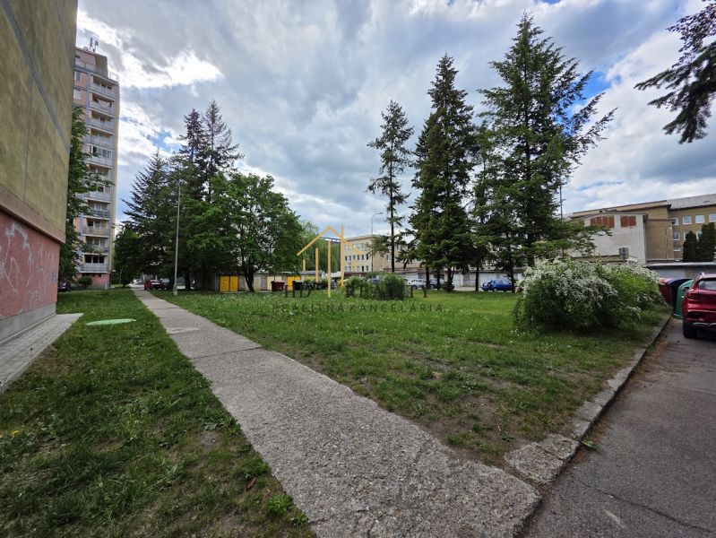In Banská Bystrica, in front of the 2-room apartment, there is greenery, a sidewalk, and trees.
