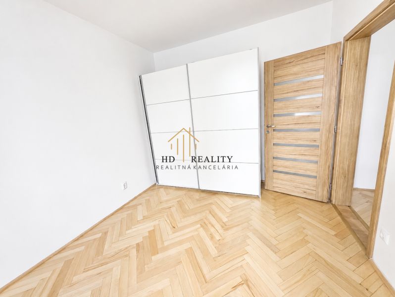 A room in a two-room apartment with a wood-patterned floor and a white wardrobe.