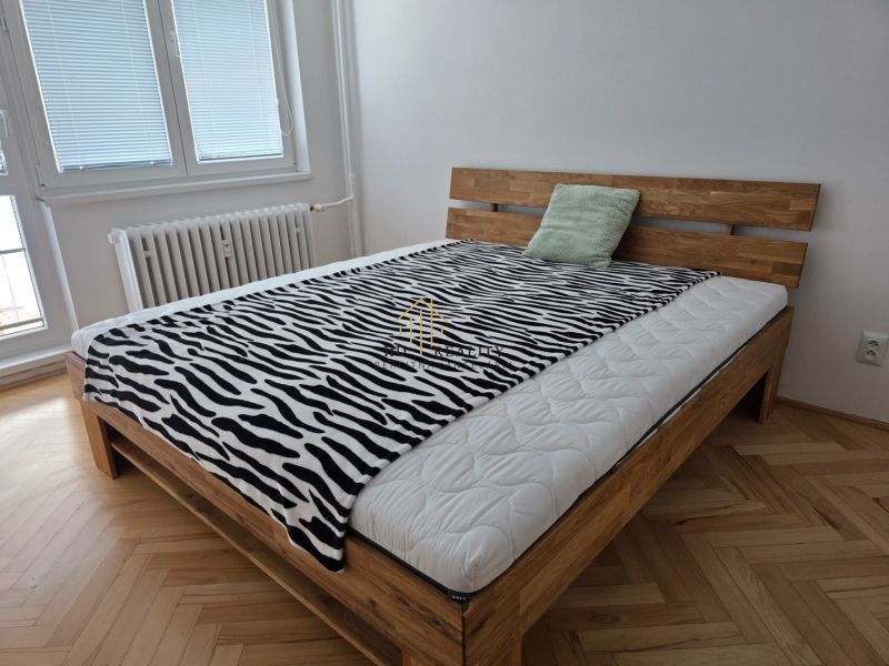 A bed with a zebra-patterned blanket in a 2-room apartment, floor with wood decor.