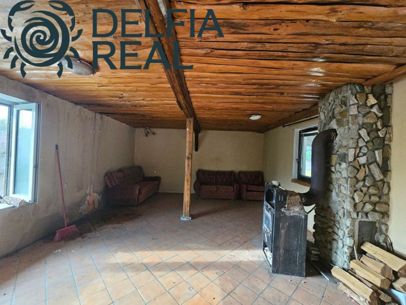 A cottage with a stone fireplace and a wooden ceiling, tiled floor, sofas.