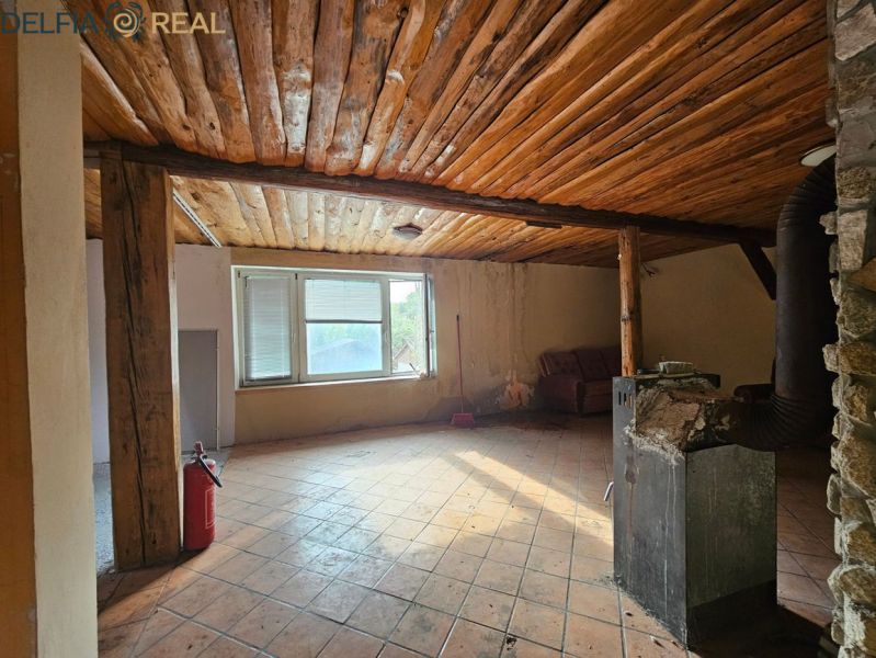 A cottage with a wooden ceiling, a stove, and a window, with a tiled floor.