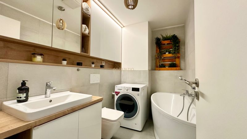 A bathroom in a 2-room apartment with a bathtub, washing machine, and sink.