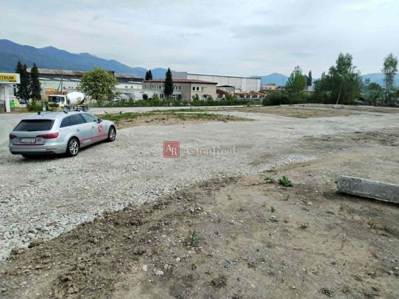 Car on a paved area between industrial buildings and mountains in Martin, Commercial land.