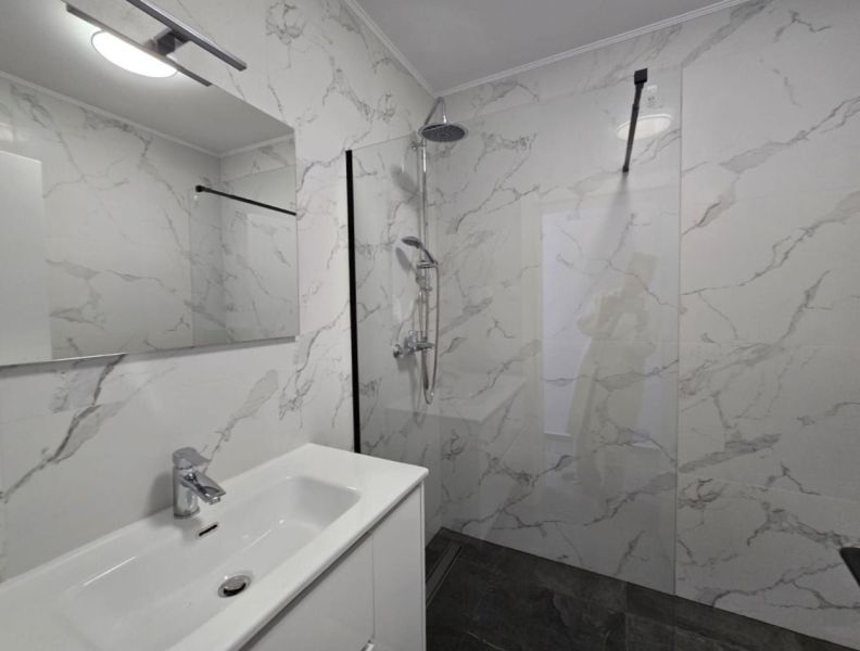 Bathroom in a family house with marble tiles, a shower, and a sink with a large mirror.