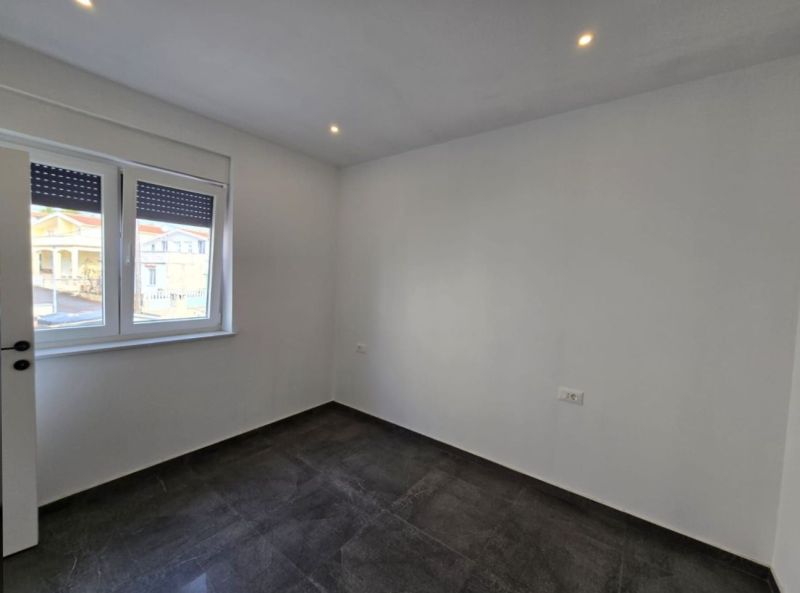 A bright room with a dark floor, white walls, and a window, Family house.