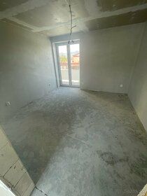 A vacant room in a three-room apartment with a concrete floor and plastered walls.