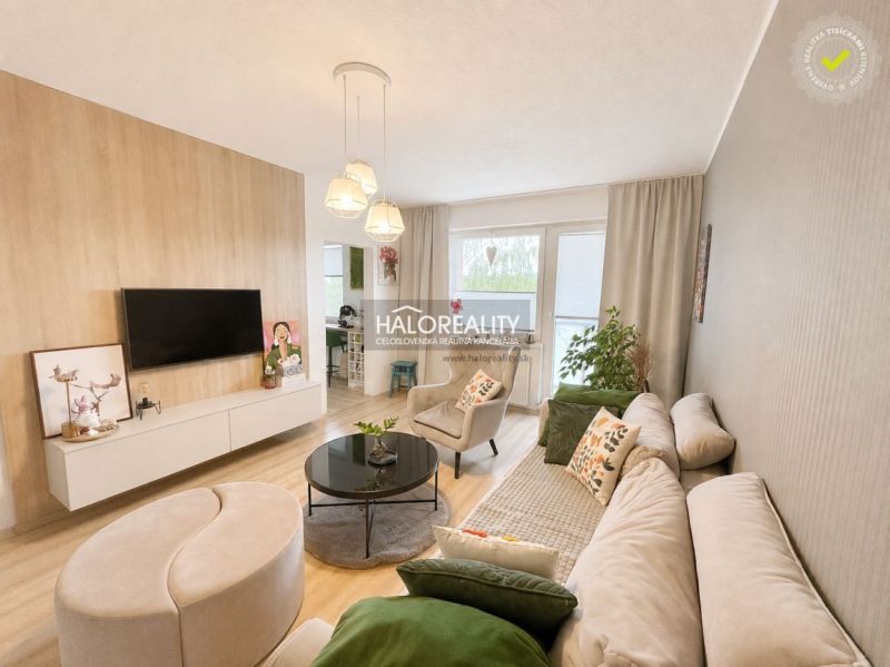 Living room of a two-room apartment with a wooden decor floor, a comfortable sofa, and a television.