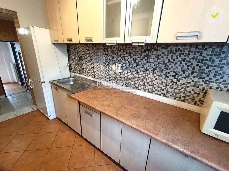 A kitchen of a three-room apartment with mosaic tiles and a wooden decor floor.