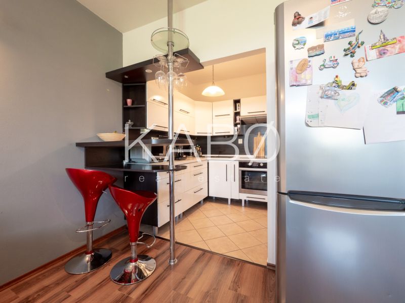 A kitchen in a 2-room apartment with bar stools and a wooden decor floor.