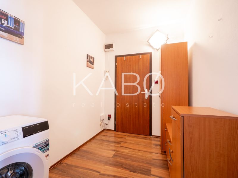 A hallway in a 2-room apartment with a wooden decor floor, a washing machine, and cabinets.