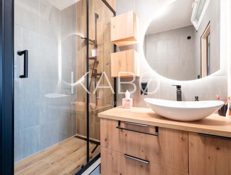 A bathroom with a shower, a sink on a wooden decor, and a round mirror.