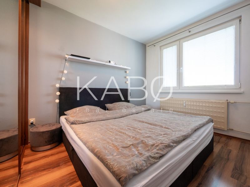 Bedroom in a two-room apartment with a wood-patterned floor and a large window.