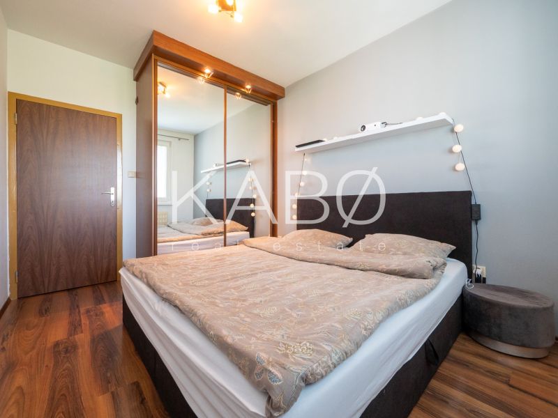 Bedroom in a 2-room apartment with a double bed, mirrored wardrobe, and wooden decor flooring.