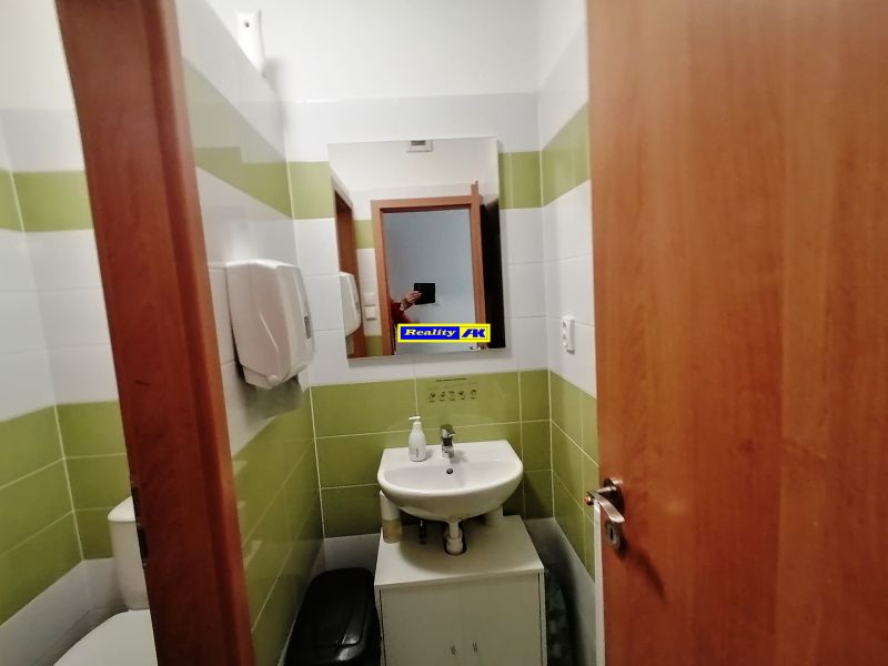 Bathroom with a sink, mirror, and green and white tiles in commercial premises.