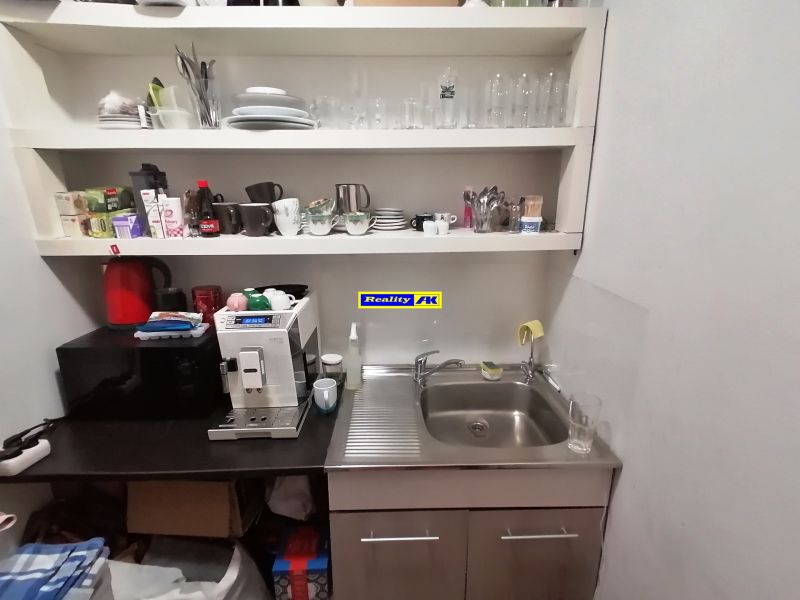 A kitchen in a commercial space with a sink, coffee maker, and shelves with dishes.