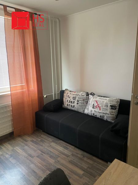A sofa with colorful cushions, orange curtains, a floor with a wooden decor, a 3-room apartment.