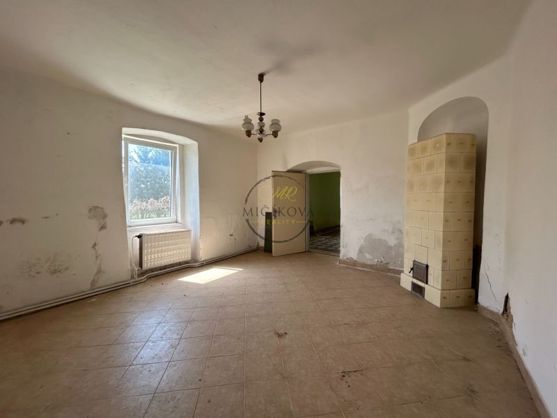 Interior of a family house with a window, white walls, and a traditional tiled stove.