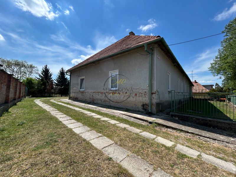 A family house in Čifáre with a lawn and a paved walkway next to a stone fence.