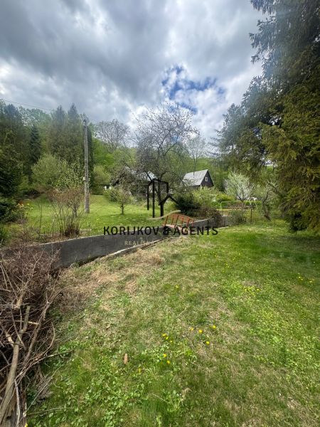 A cottage in Svinica surrounded by greenery and trees, with a cloudy sky.