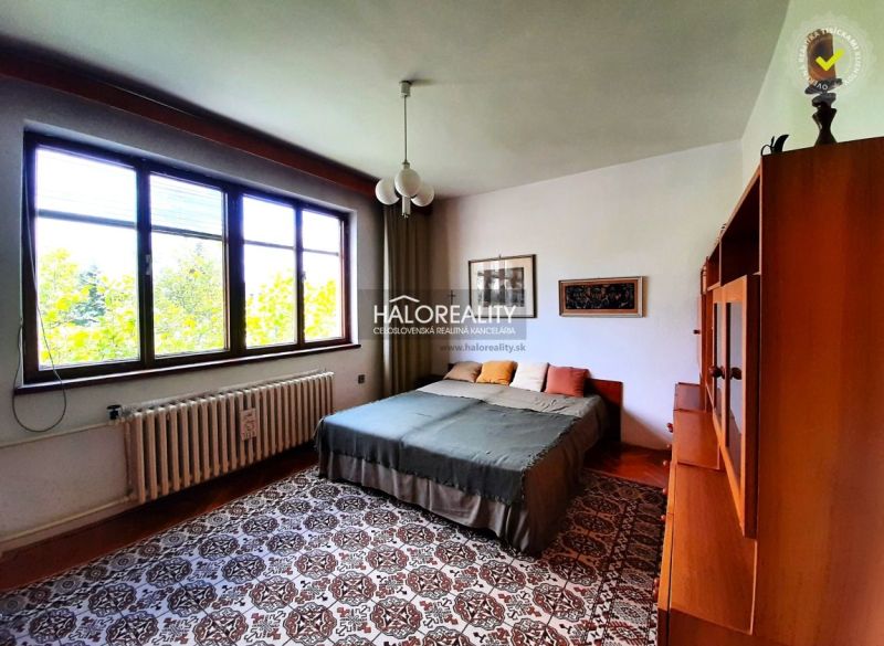 Bedroom in a family house with large windows, carpet, and a bed with pillows.