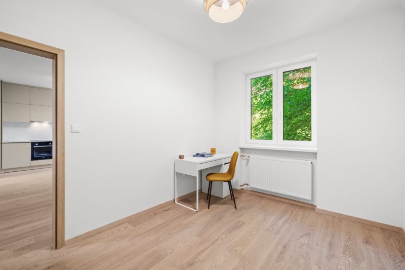 A room in a 3-room apartment with a desk, chair, and a wooden decor floor.