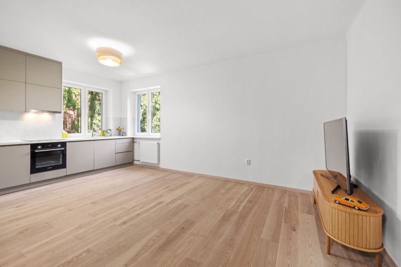 A spacious kitchen in a 3-room apartment with a wooden decor floor and minimalist furniture.