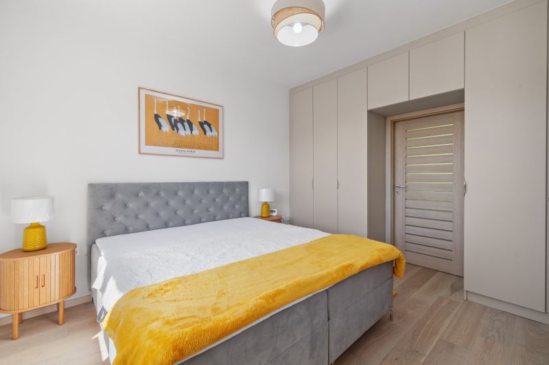 Bedroom with a bed, yellow blanket, painting, and a large built-in wardrobe in a 3-room apartment.
