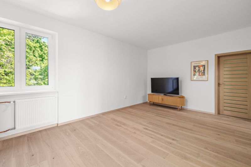 Living room in a 3-room apartment with a TV, cabinet, and wooden decor flooring.