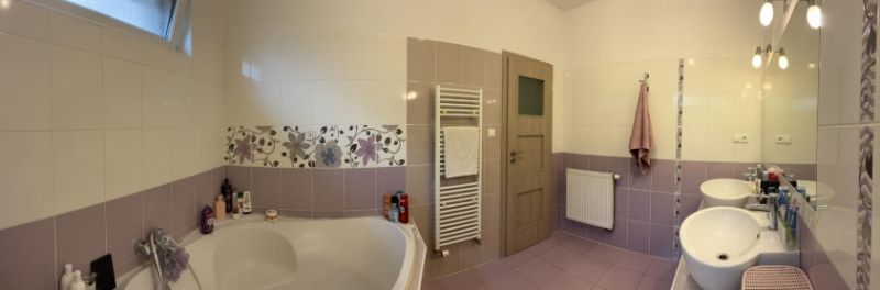A bathroom in a family house with a wide bathtub, double sink, patterned tiles, and a large mirror.
