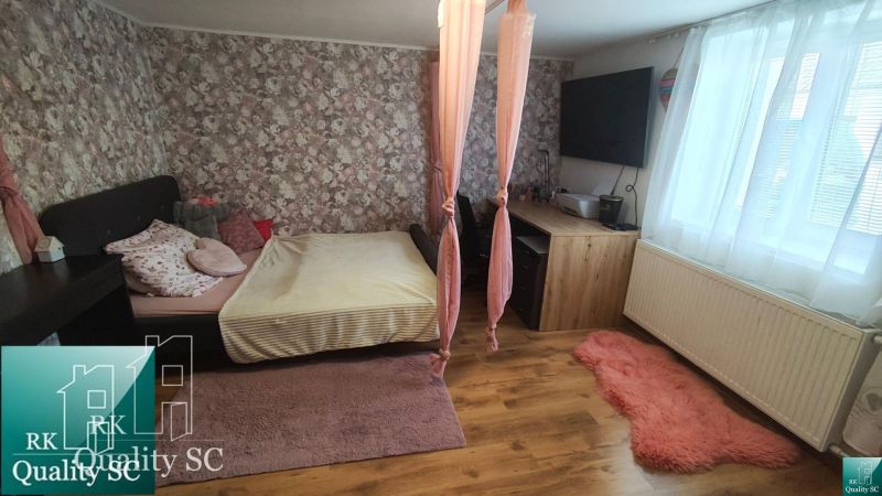 A bedroom in a family house with floral wallpaper, a bed, and a wooden decor floor.
