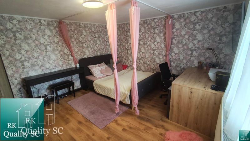 A bedroom in a family house with floral wallpaper, a bed, and a wooden decor floor.