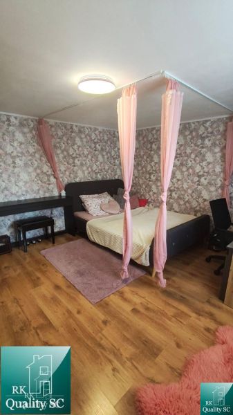 A bedroom in a family house with romantic pink details and a wood-patterned floor.