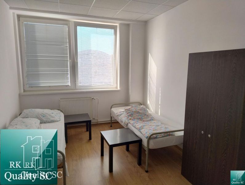 A room with a light wooden floor, beds, and dark furniture in warehouses and halls.