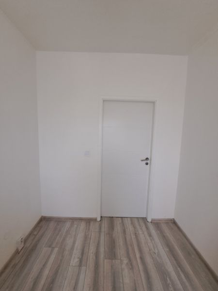 A white room in a 3-room apartment with wood-patterned flooring and white doors.