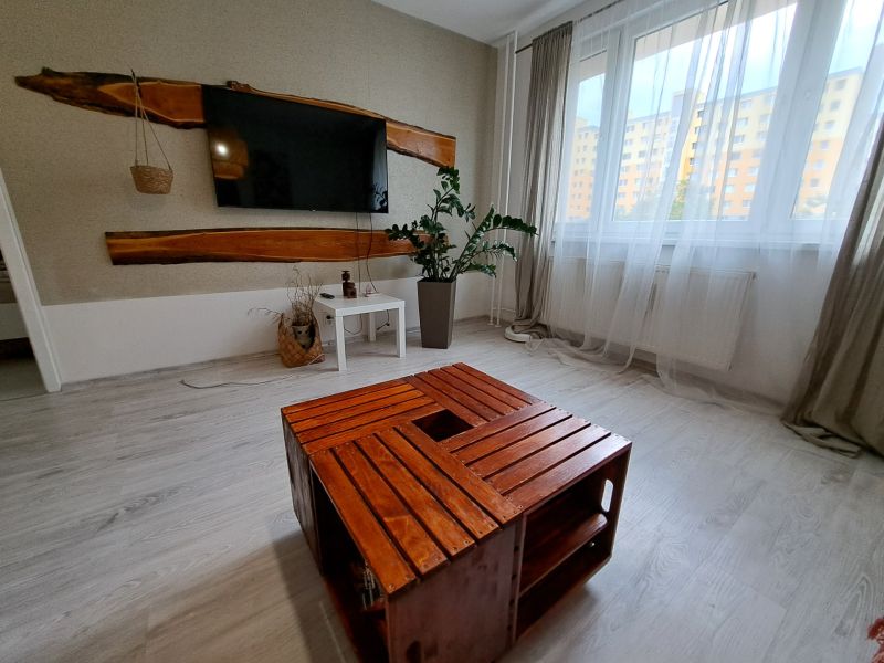 Living room in a 3-room apartment with a television, wooden table, and white curtains.